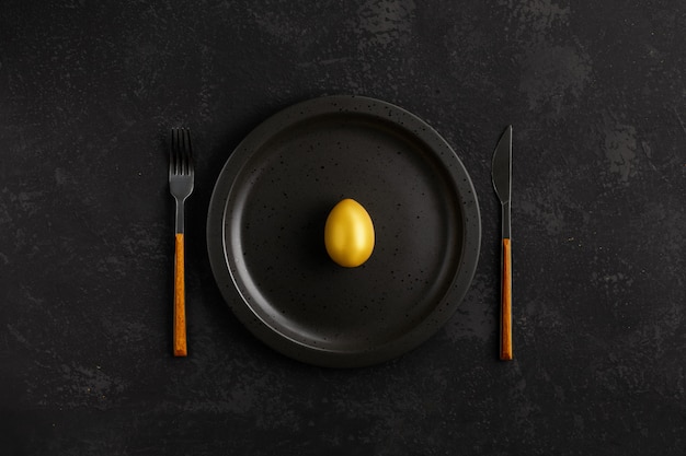 Wielkanocny pojęcie z Złotym jajkiem na czarnym talerzu nad czarnym łupku, kamienia lub betonu tłem. Widok z góry z miejsca kopiowania.