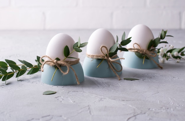 Wielkanocny świąteczny nakrycie stołu z białymi jajkami kurzymi w filiżankach jaj, gałązkami liści eukaliptusa. .