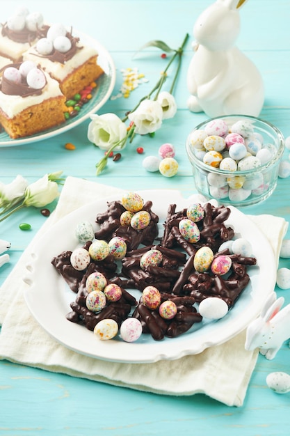 Wielkanocny tort czekoladowy z mini czekoladowymi jajkami cukierkowymi z kwitnącymi kwiatami wiśni lub jabłek na niebieskim tle Stół Kreatywny przepis na stół wielkanocny z ozdobami świątecznymi