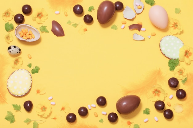 Wielkanocny żółty tło z czekoladowymi jajkami, cukierkiem i spri