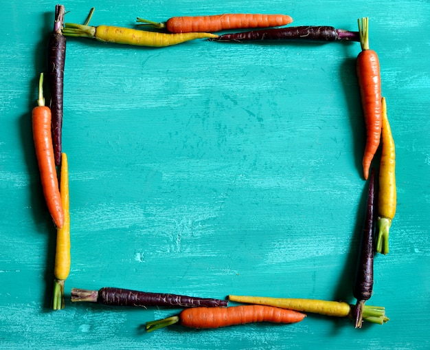 Zdjęcie wielobarwne marchewki otaczające kwadrat na drewnie w kolorze turkusowym