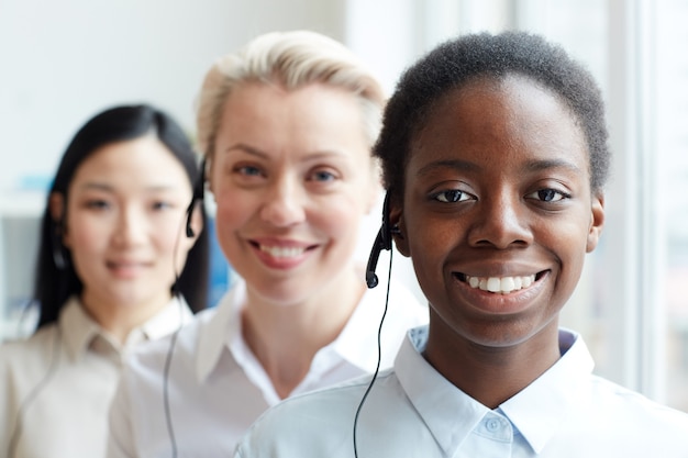 Wieloetniczna grupa kobiet operatorów call center patrząc stojących w rzędzie, skupić się na uśmiechniętej African-American kobiety noszącej zestaw słuchawkowy na pierwszym planie