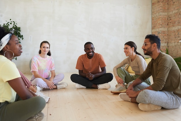 Wieloetniczna grupa ludzi siedzących na podłodze i dyskutujących ze sobą