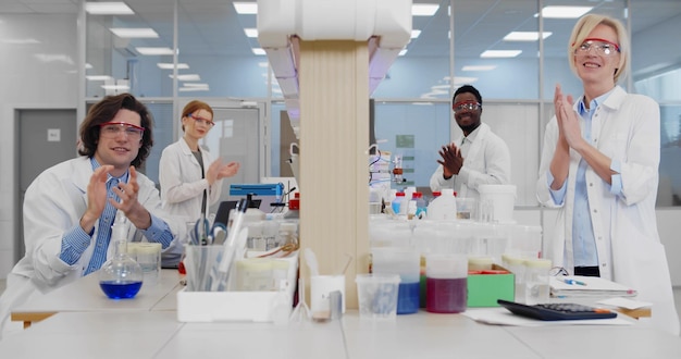 Wieloetniczna grupa naukowców medycznych oklaskuje razem uśmiechając się do kamery w nowoczesnym laboratorium