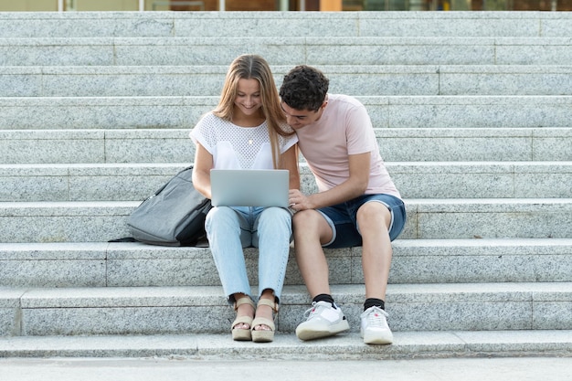 Wieloetniczna para nastolatków pracujących razem na laptopie i siedząca na schodach