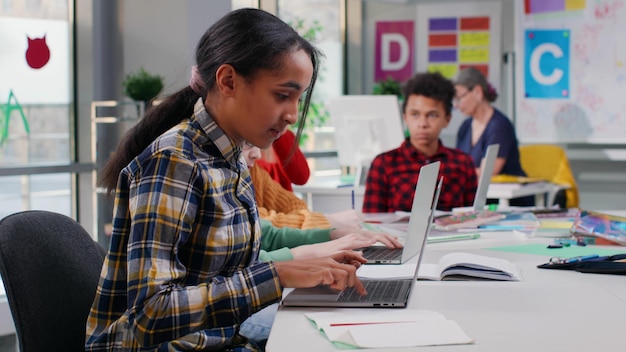 Wieloetniczne nastolatki uczą się na laptopie w klasie komputerowej