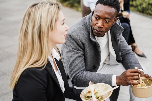 Wieloetniczni ludzie biznesu robiący sobie przerwę na lunch na świeżym powietrzu z biurowca. Skoncentruj się na twarzy afrykańskiego mężczyzny