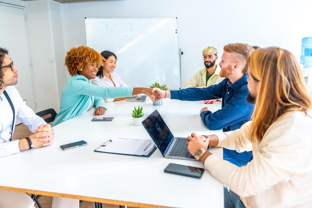 Wieloetniczni ludzie ściskają ręce siedząc w pokoju coworkingowym