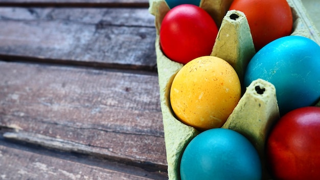 Wielokolorowe jajka malowane gwaszem i skórką cebuli w kartonowym pudełku na tle drewnianego stołu Dziesięć gotowanych jajek Pocztówka plakat na Wielkanoc Wielkanoc czerwony niebieski żółty brązowy jaja