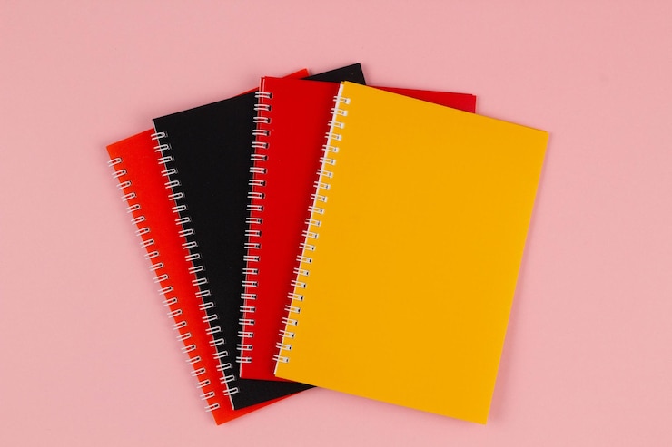 Zdjęcie wielokolorowe notebooki czarno-czerwone i pomarańczowe na różowym tle z przestrzenią do kopiowania tekstu górna