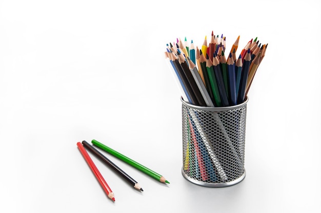 Wielokolorowe ołówki w szarym metalowym szkle i kilka ołówków na białym tle