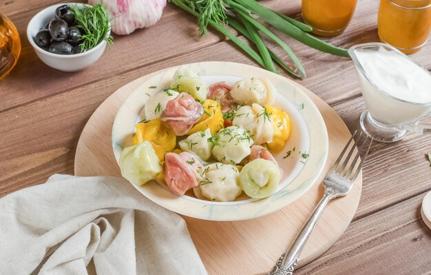 Wielokolorowe pierogi dla dzieci z mięsem na białym talerzu na ciemnym drewnianym tle