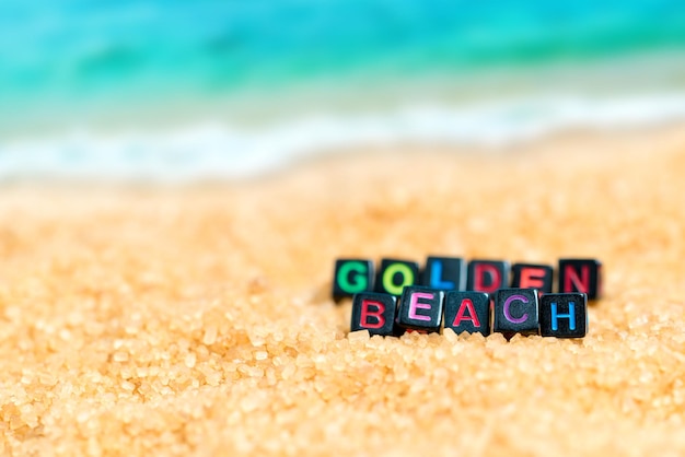 Wielokolorowe słowo GOLDEN BEACH z czarnych kostek w piasku na tle plaży i morza