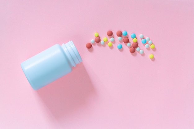 Wielokolorowe tabletki pigułki kapsułki w plastikowej butelce na różowym tle kopii przestrzeni
