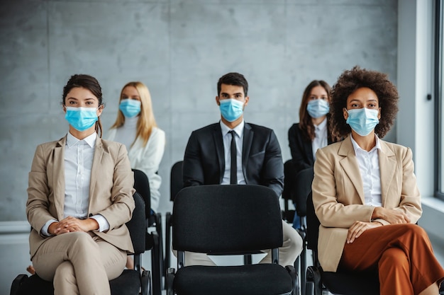 Wielokulturowa grupa ludzi biznesu z maskami na twarz siedząca na seminarium i słuchająca podczas koronawirusa.