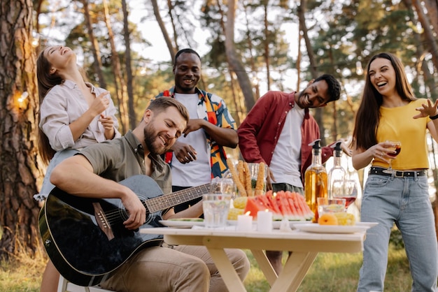 Zdjęcie wielokulturowa grupa ludzi brodaty hipster grający na gitarze i przyjaciele tańczący i bawiący się