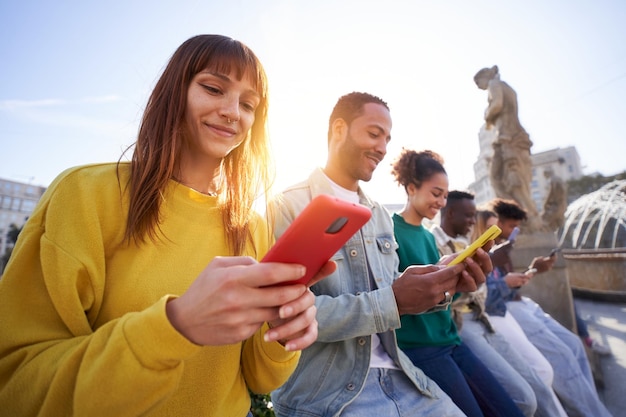 Wielokulturowa grupa uśmiechniętych przyjaciół używających telefonów komórkowych na zewnątrz ludzie i uzależnienie od technologii