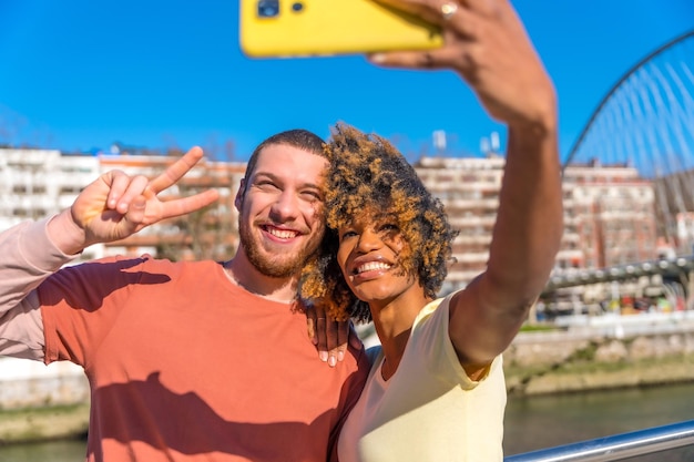 Zdjęcie wielorasowa para ulicami miasta styl życia selfie uśmiechając się nad rzeką