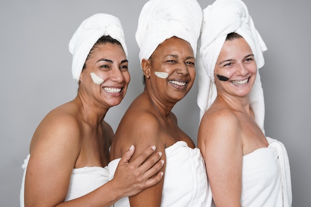 Wielorasowe dojrzałe kobiety robiące razem zabiegi kosmetyczne na skórę