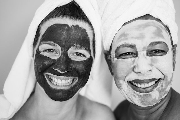 Wielorasowe starsze kobiety wykonujące zabiegi upiększające przy użyciu maski skórnej. Skup się na lewych kobiecych oczach. Edycja czarno-biała