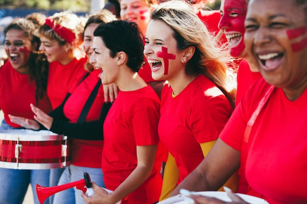 Wielorasowi czerwoni fani sportu krzyczą, wspierając swoją drużynę Kibice piłki nożnej bawią się na imprezie konkursowej Skup się na środkowej twarzy dziewczyny