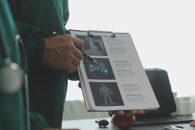 Wielorasowy zespół lekarzy omawiających pacjenta stojącego zgrupowanego w holu, patrzącego na komputer typu tablet z bliska