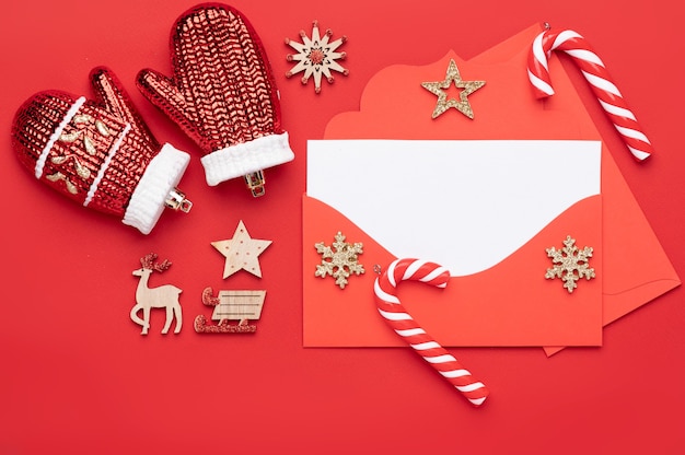 Wieniec bożonarodzeniowy Dekoracja bożonarodzeniowa na czerwonym tle składająca się z czerwonej koperty z pustym białym papierem firmowym na tekst i ozdobiona świątecznymi cukierkami