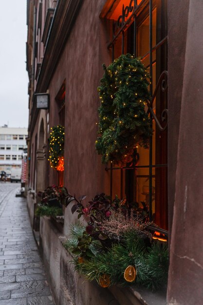 Wieniec świąteczny na oknie restauracji Piękny dom wakacyjny ozdobiony jest iglastymi wieńcami i girlandami Wieniec świąteczny z choinkami i girlandami na tle czerwonego domu