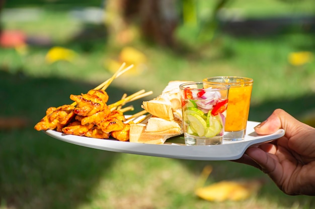 Wieprzowina Satay Z Mlekiem Kokosowym I Chlebem Z Sosem Orzechowym Na Białym Plastikowym Talerzu W Dłoni.