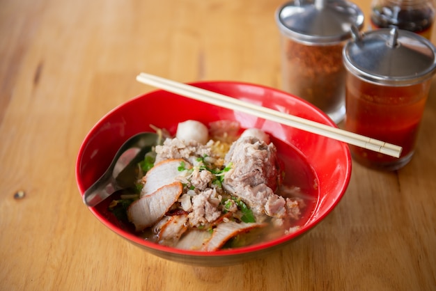 Zdjęcie wieprzowina tom yum noodle w czerwonej misce, łyżce i pałeczkach