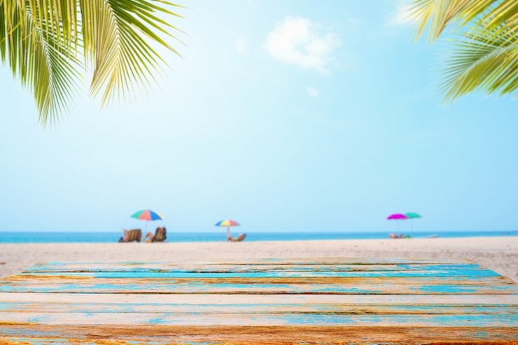 Zdjęcie wierzchołek drewno stół z seascape, palmowym liściem, spokojnym morzem i niebem przy tropikalną plażą