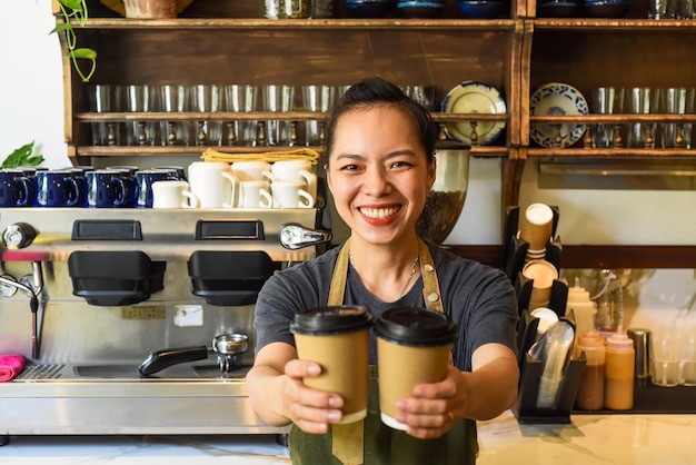 Wietnamska uśmiechnięta kelnerka trzyma papierowe filiżanki z kawą w kawiarni