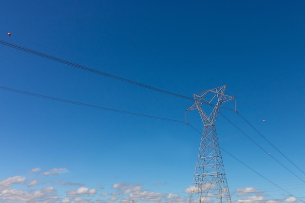 Wieża wysokiego napięcia przesyłu energii w okolicy na białym tle o zachodzie słońca z kilkoma ładnymi ciepłymi chmurami na niebie. Letnia fotografia miejska.