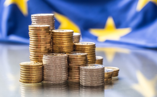 Zdjęcie wieże z monetami euro i flagą unii europejskiej w tle.