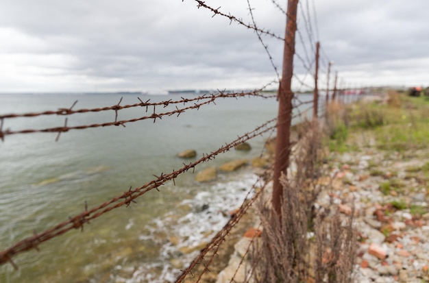 Zdjęcie więzienie, koncepcja ograniczenia - ogrodzenie z drutu kolczastego nad szarym niebem i morzem