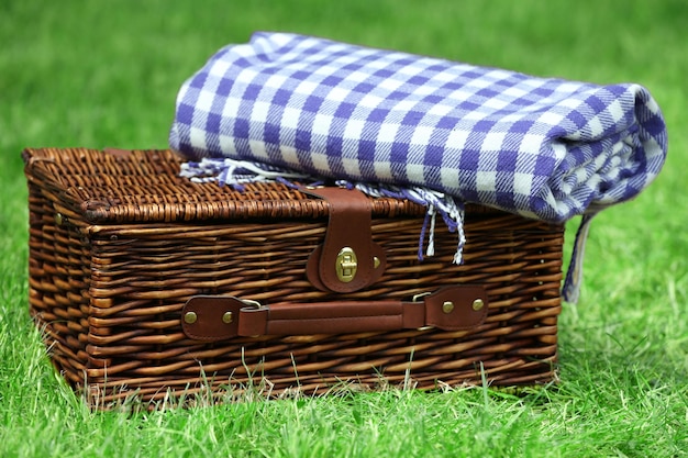 Wiklinowy kosz piknikowy i krata na zielonej trawie na zewnątrz