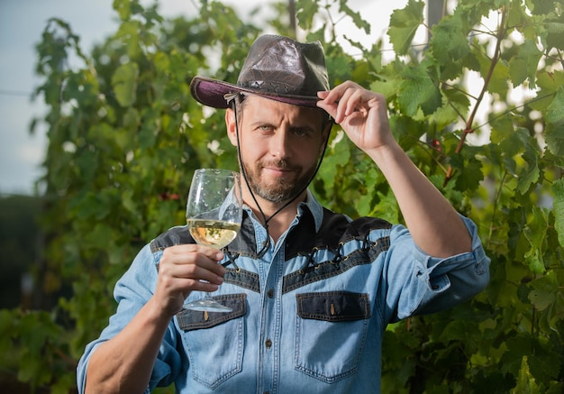 Winnica pije mężczyzna właściciel winnicy zawodowy winiarz na farmie winogron wita brodaty mężczyzna w kapeluszu z kieliszkiem enolog z kieliszkiem sommelier rolnik pije wino na zdrowie