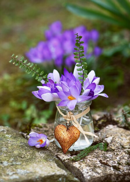 Zdjęcie wiosenna aranżacja kwiatów z fioletowymi kwiatami krokusów w małym szklanym wazonie z zardzewiałym wisiorkiem sercowym