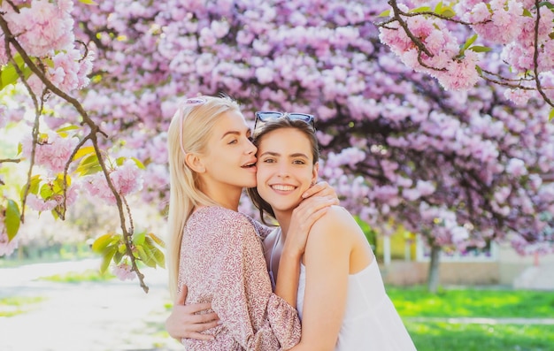 Wiosenne dziewczyny w kwiatach Plenerowy portret młodej pięknej, szczęśliwej uśmiechniętej pary kobiet pozujących w pobliżu