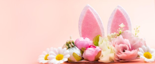 Wiosenne wakacje kreatywne tło z uszami królika ozdobione kwitnącymi kwiatami na pastelowym różowym motywie Kreatywna kopia przestrzeń Wielkanocna koncepcja