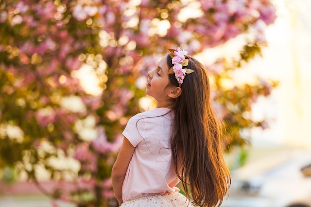 Wiosenny portret, urocza dziewczynka tańczy w pobliżu drzewa sakura o zachodzie słońca