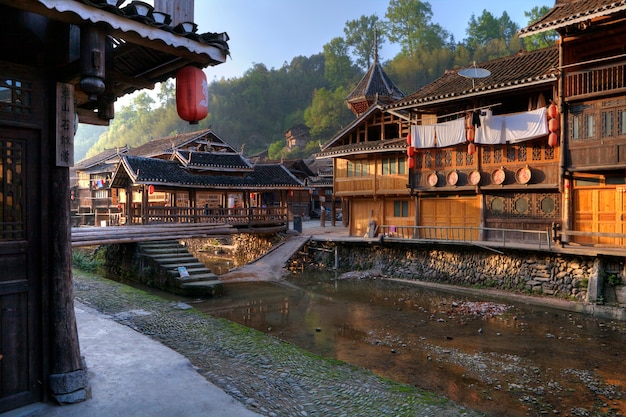 Wioska Zhaoxing Dong, Prowincja Guizhou, Mniejszości Etniczne W Południowo-zachodnich Chinach W świetle Zachodzącego Słońca, Drewniany Dom I Zadaszony Most Nad Rzeką Wiejską.