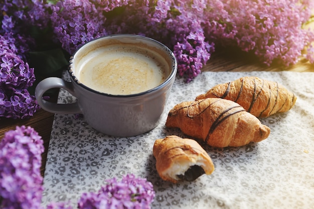 Wiosna Cet i świeże śniadanie na drewnianym stole. Na stole są spokojne rogaliki i filiżanka cappuccino. Bukiet bzu na drewnianym stole.