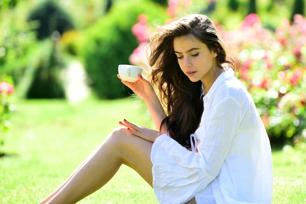 Wiosna Kobieta w letnim polu z kawą Szczęśliwa dziewczyna na zewnątrz w ogrodzie różanym Kobieta cieszy się na świeżym powietrzu