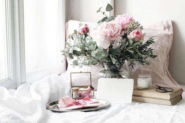 Zdjęcie wiosna lato ślub martwa scena pusta papierowa karta makieta stare książki i lniana poduszka na parapecie vintage kobieca kompozycja kwiatowa bukiet różowych róż kwiaty piwonii i eukaliptusa