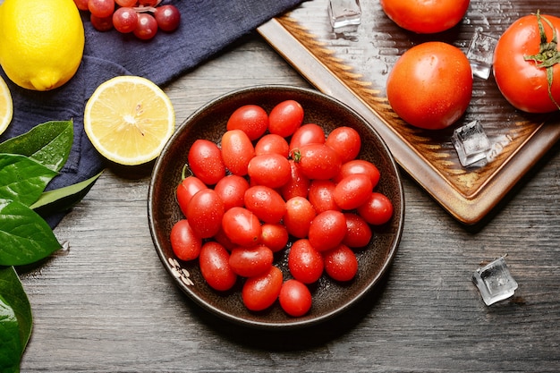 Wiśniowe pomidory na drewnianym talerzu i tle drewniany stół