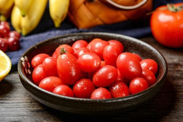 Wiśniowe pomidory na drewnianym talerzu i tle drewniany stół