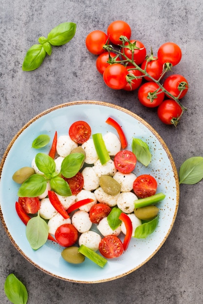 Wiśniowe pomidory, ser mozzarella, bazylia i przyprawy na szarej tablicy łupkowej. Składniki sałatki włoskiej tradycyjnej caprese. Jedzenie środziemnomorskie.