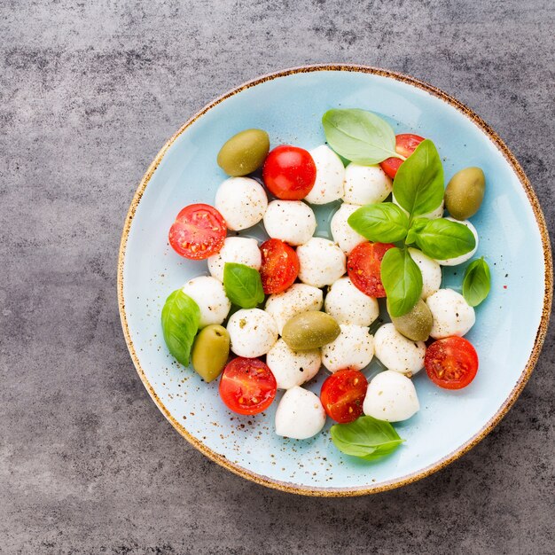 Wiśniowe pomidory, ser mozzarella, bazylia i przyprawy na szarej tablicy łupkowej. Składniki sałatki włoskiej tradycyjnej caprese. Jedzenie środziemnomorskie.