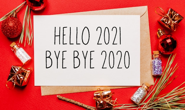 Zdjęcie witam 2021 pa pa pa 2020 świąteczna notatka z prezentem, gałązką jodły i zabawką na czerwono na białym tle. koncepcja nowego roku